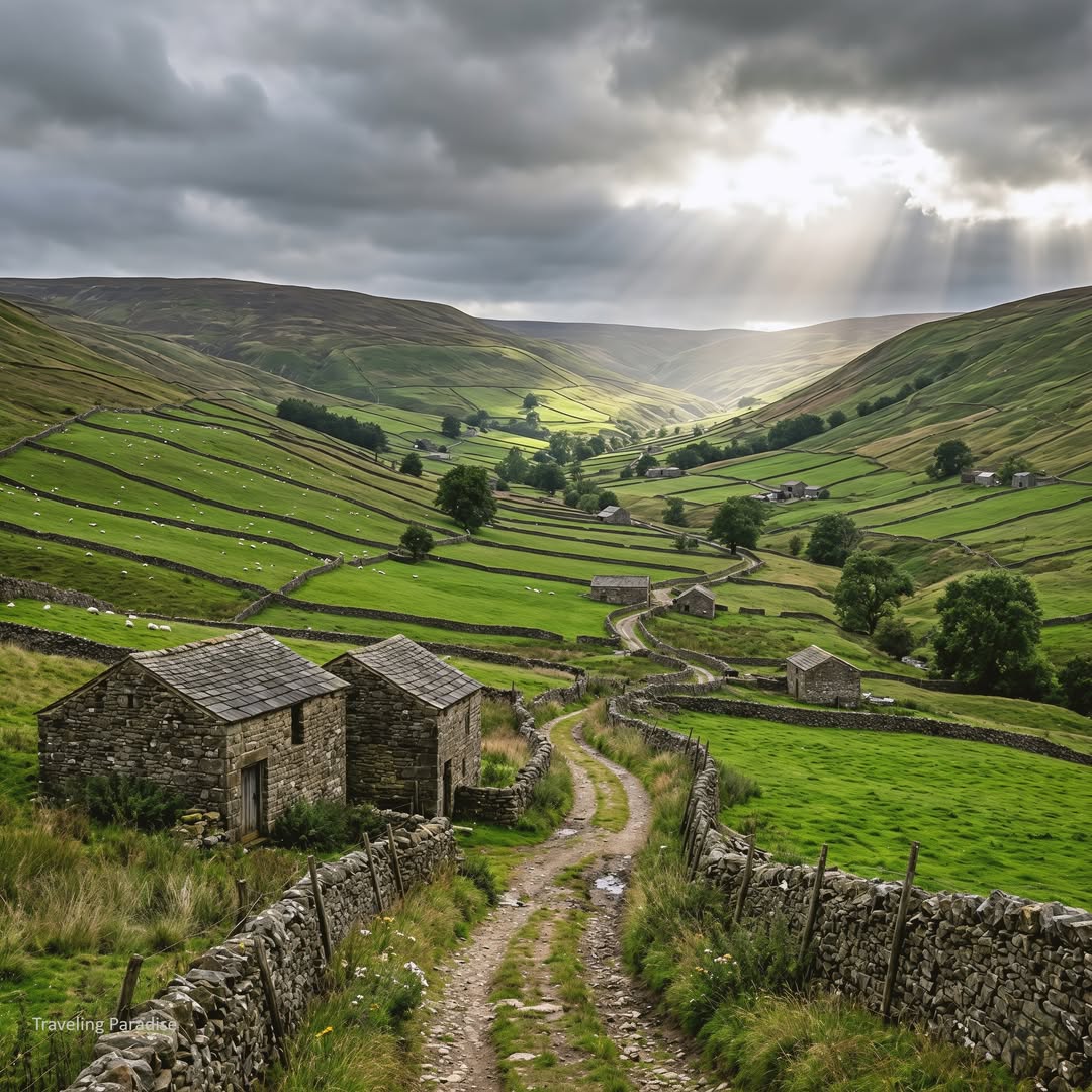 Stone farmhouses and a winding dirt road in a green valley beneath dramatic cloudy skies