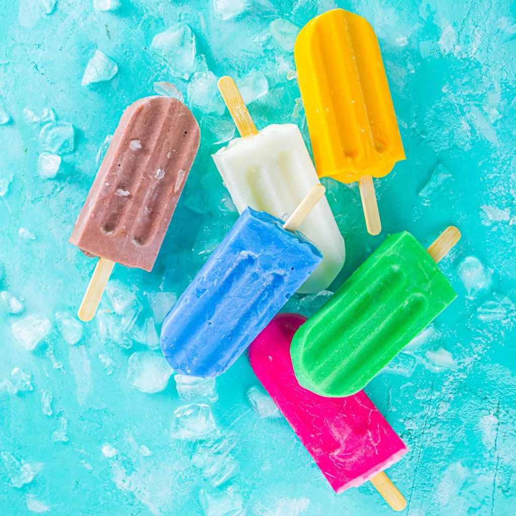 Colorful frozen popsicles on wooden sticks scattered over bright blue crushed ice