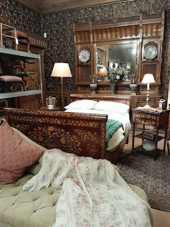 Victorian bedroom with ornate carved wooden bed, antique furniture, patterned wallpaper, and period lamps