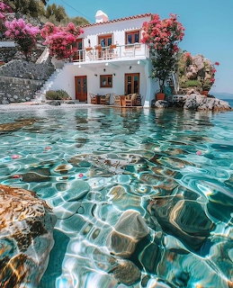 White Greek villa with pink bougainvillea trees beside crystal clear turquoise sea water