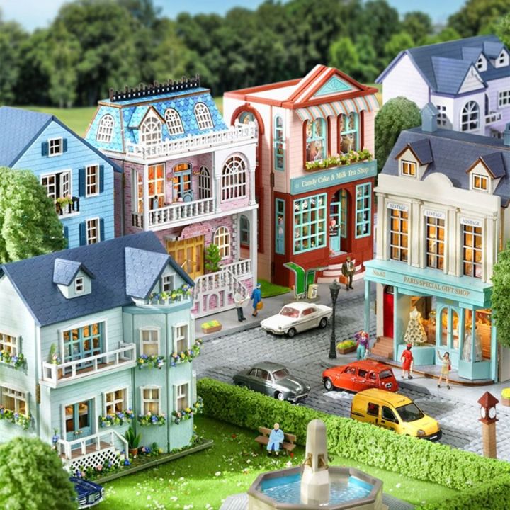 Aerial view of miniature dollhouse village with colorful Victorian houses, fountain, and toy cars