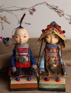 Two handcrafted Mongolian Ulger dolls in traditional costumes with ornate headdresses on wooden stands