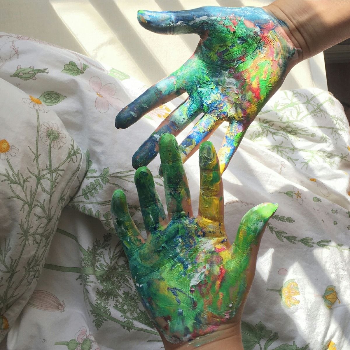 Two hands covered in colorful paint over white floral fabric