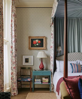 Elegant bedroom with canopy bed, floral curtains, nightstand with red vase lamp, and framed flower artwork on wall