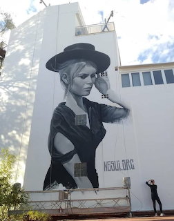 Monochromatic street art mural of woman in hat on white building facade