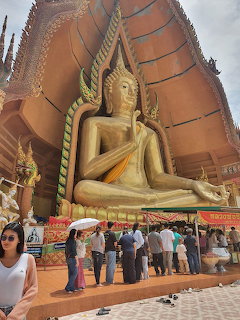 Large golden Buddha statue at a Thai temple entrance with visitors standing below