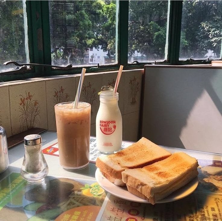 Iced coffee, milk bottle, and toasted sandwiches on a sunlit table by a window