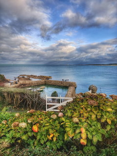 Small stone harbor with turquoise water at Port Racine surrounded by green vegetation and cloudy sky