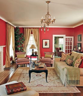 Living room with red walls, patterned chairs, cream sofa, chandelier, and gold curtains