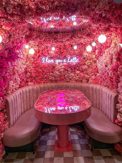 Pink rose-covered cafe booth with neon sign reading I Love You a Latte and curved velvet seating