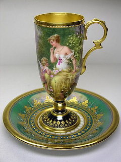 Ornate porcelain cup and saucer with gold trim and painted pastoral scene of woman and cherub