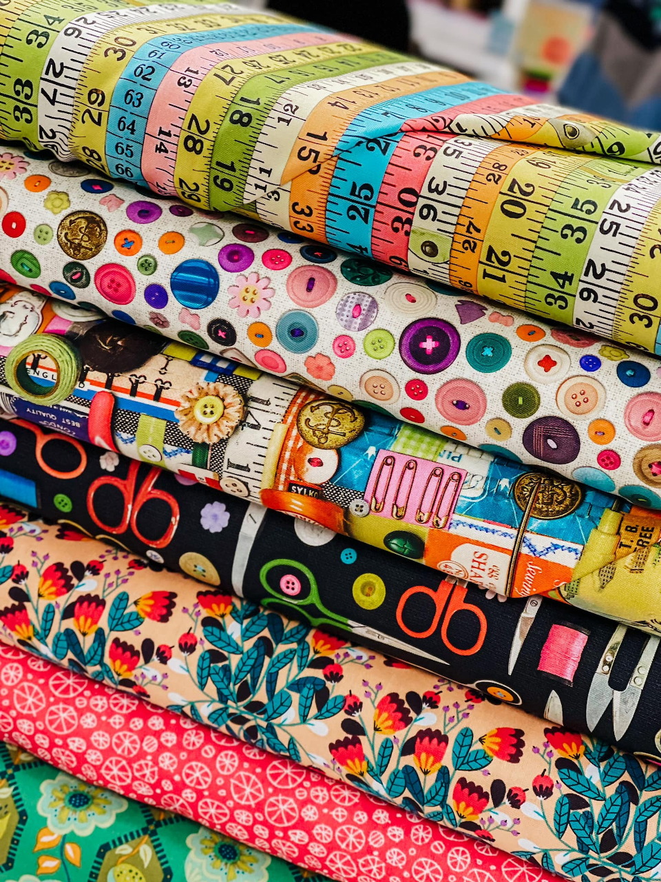 Stack of colorful quilting fabric rolls with measuring tape and decorative button patterns