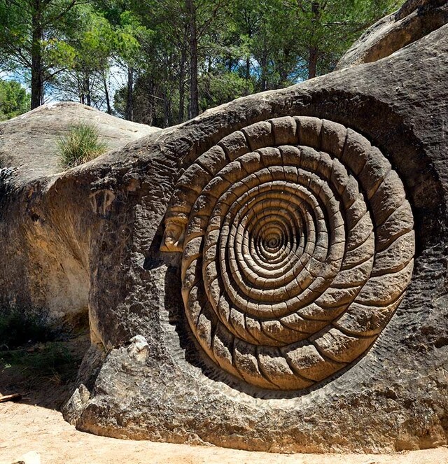 Spiral carving sculpted into a large rock outdoors with trees in the background