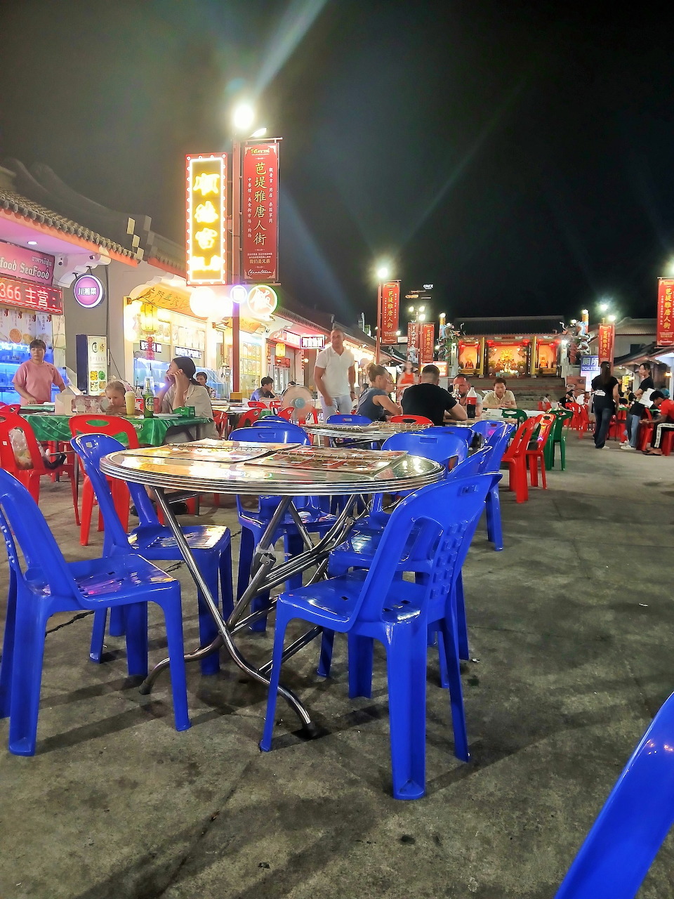 Blue plastic chairs and tables at an outdoor Asian night market with lit food stalls and Chinese signs