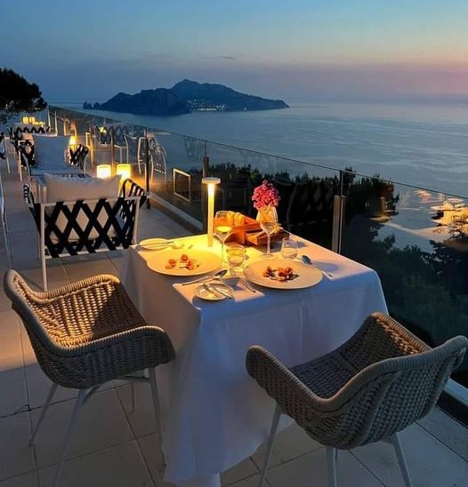 Outdoor dining table on terrace overlooking Capri island at sunset with ocean and mountain views