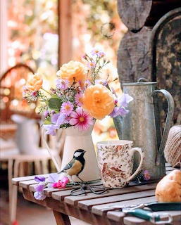 Chickadee bird next to vibrant flower bouquet with teacups on wooden surface