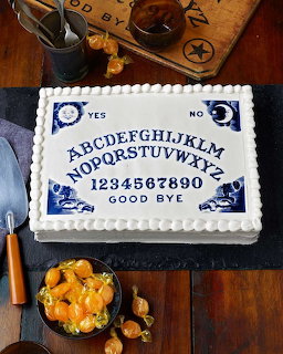 Rectangular white cake decorated as a Ouija board on a wooden table with Halloween props