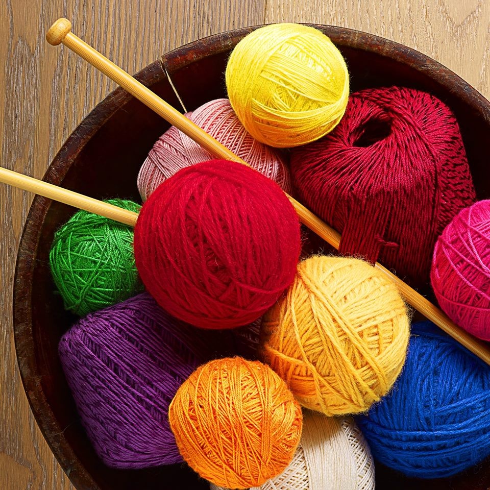 Wooden bowl containing colorful yarn balls and knitting needles on textured surface