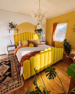 Bright yellow velvet bed in a bohemian bedroom with plants, patterned rug, and bubble chandelier