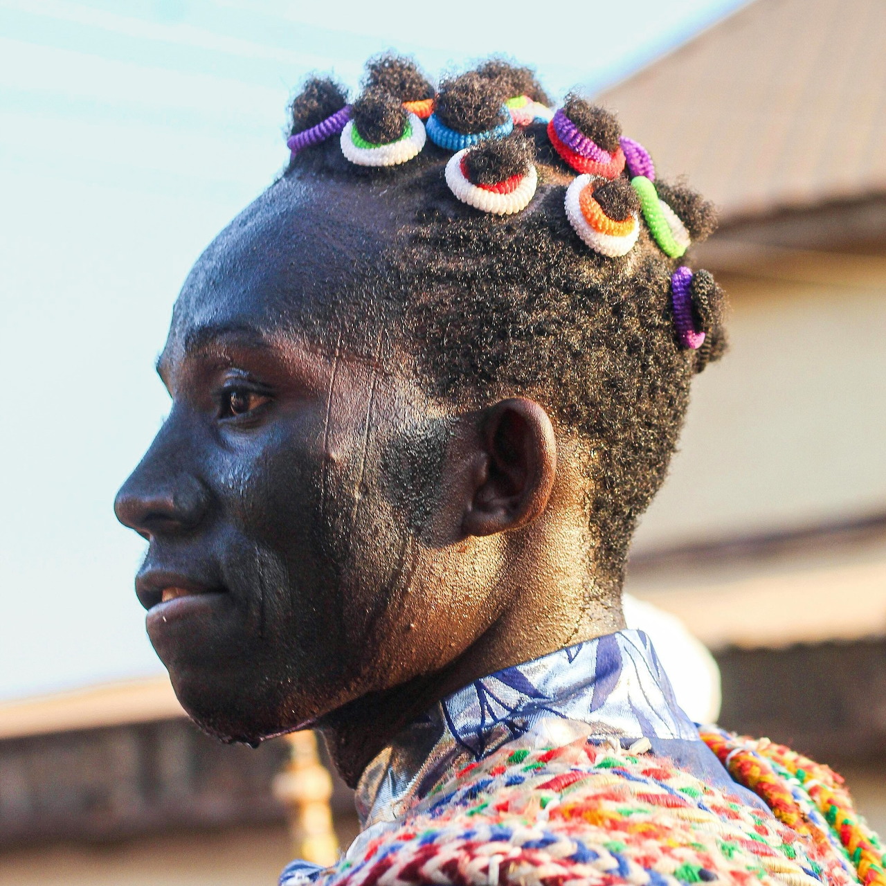 Side profile of African man with colorful beaded hairstyle and traditional decorative accessories
