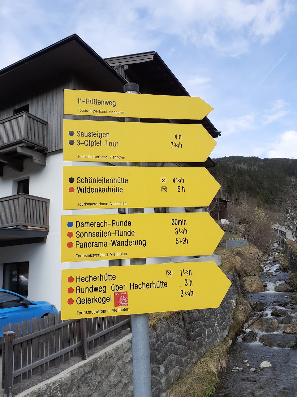 Yellow hiking trail signpost in Austria with multiple directional arrows and trail names in German
