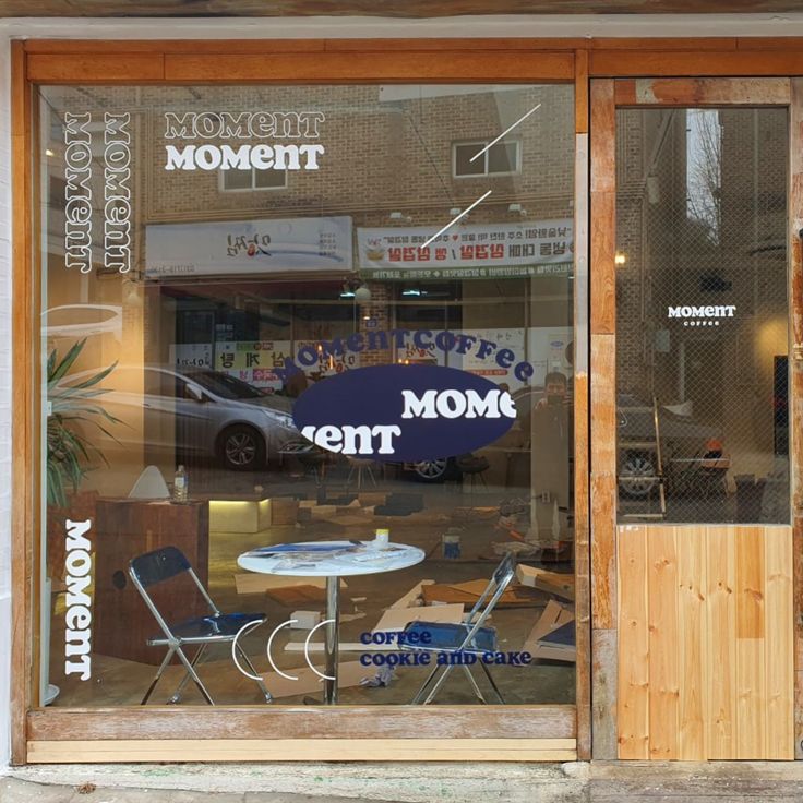 Wood-framed cafe storefront window with tables, chairs, and a car reflected in the glass