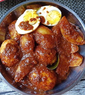 Wooden bowl of rendang with eggs and potatoes in dark brown curry sauce