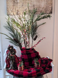Christmas arrangement with pine branches, red berries, plaid blanket, small gifts, and angel figurine on a table