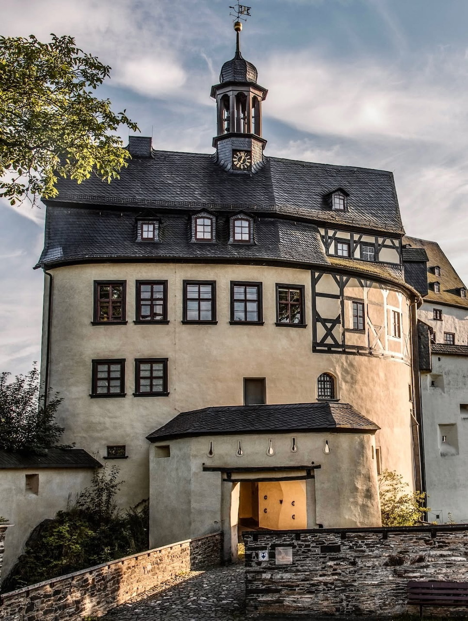 Historic castle with white walls, dark roof, clock tower and arched entrance against cloudy sky