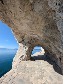 Natural rock arch over a stone-paved coastal path with blue sea visible through the opening