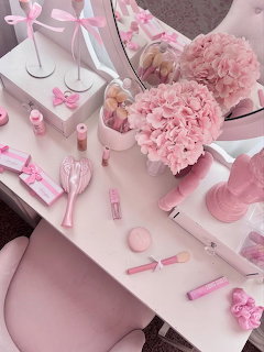 Pink vanity desk with hydrangea flowers, makeup products, ribbons, and decorative accessories in pastel pink