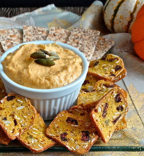 Pumpkin dip in white bowl with sliced pumpkin bread and whole pumpkin on wooden cutting board