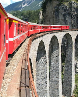Red train crossing a stone viaduct in the Swiss mountains