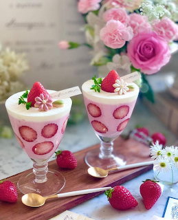 Two pink strawberry mousse desserts in patterned glass cups topped with strawberries and flowers