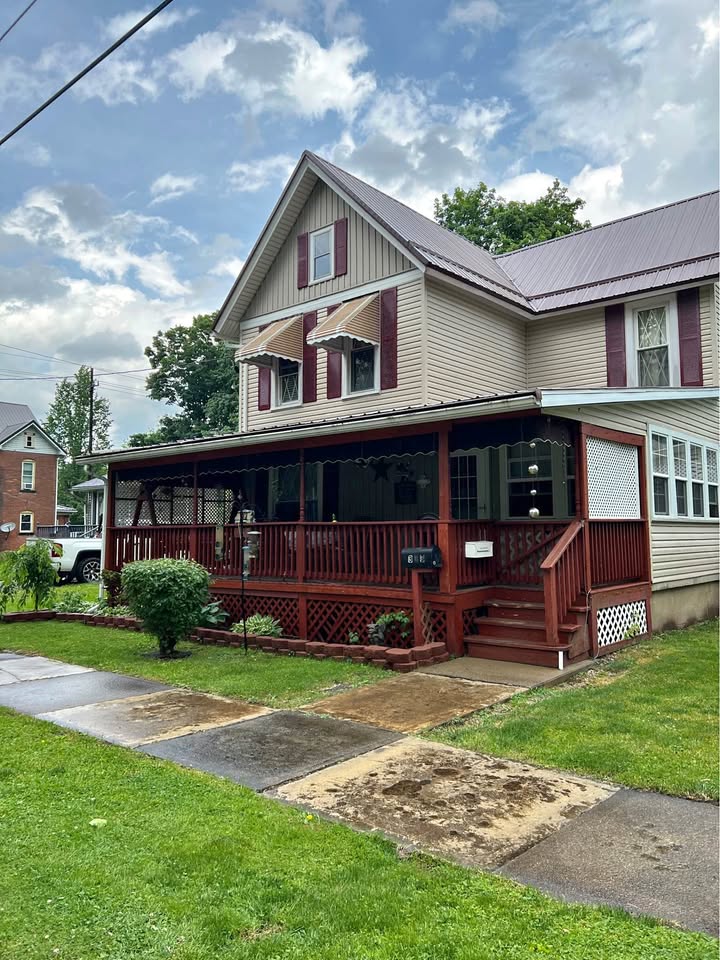 Two-story beige and brown cottage with covered porch and green lawn on a residential street