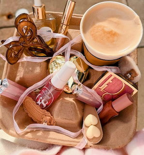 Cardboard tray with latte, lip products, perfume bottle, blush compact, and hair claw clip