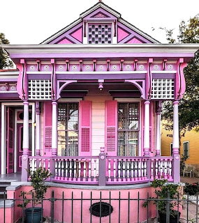 Ornate pink Victorian house with white porch railings and decorative shutters