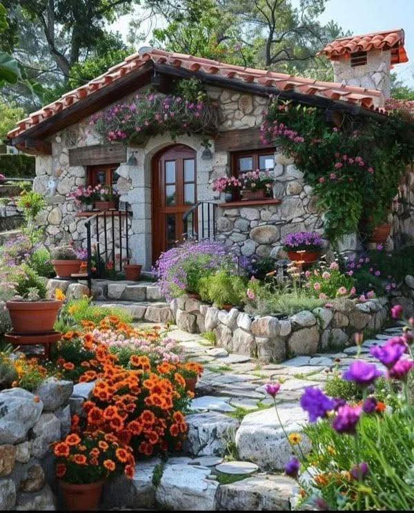 Stone cottage with wooden door and windows surrounded by colorful flowers and stone garden path