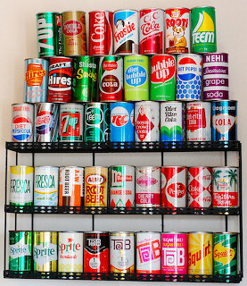 Shelves displaying rows of colorful vintage soda and soft drink cans from various brands