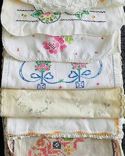Stack of vintage embroidered linen pieces with floral patterns and lace trim