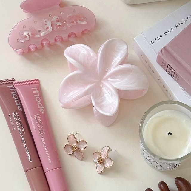 Pink beauty products and accessories arranged in flatlay composition with flower dish and candle