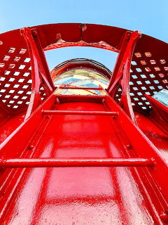 Upward view of red and white striped lighthouse tower with lattice gallery platform