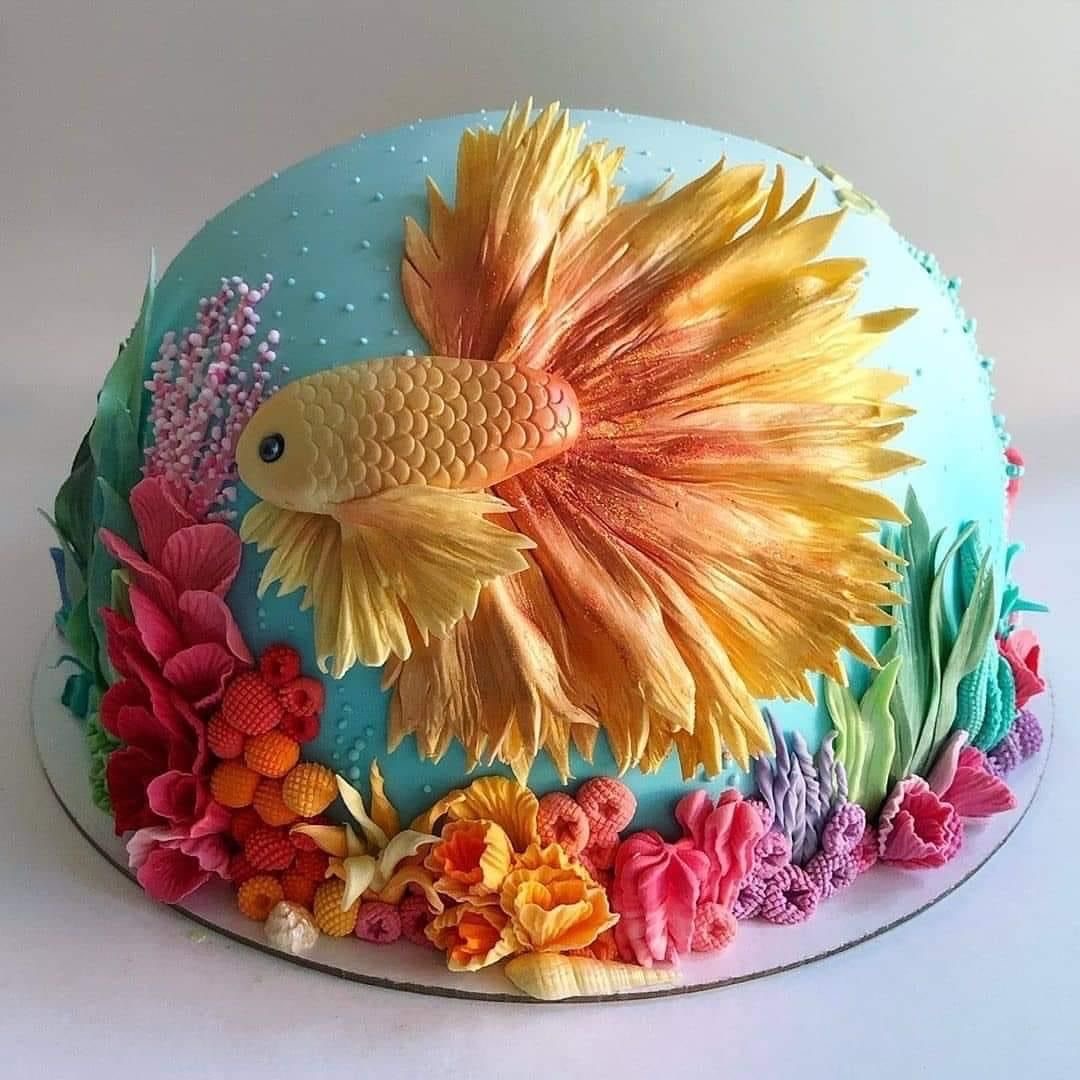 Blue cake with a golden betta fish design and colorful frosting flowers