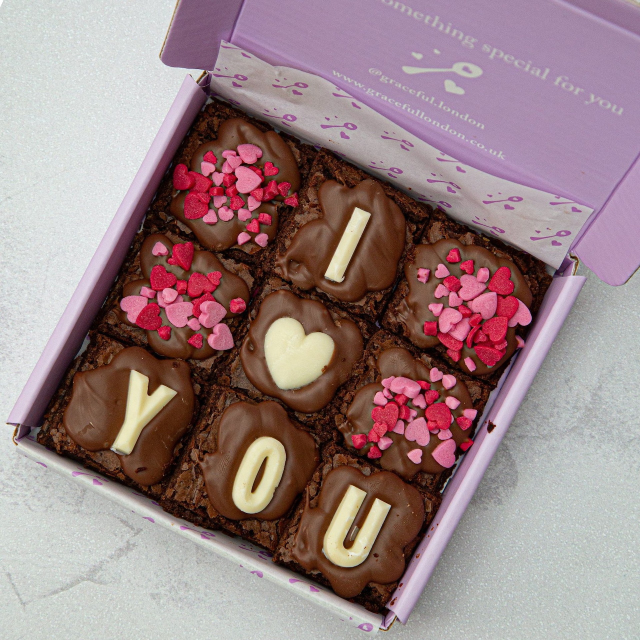 Box of chocolate brownies decorated with pink heart sprinkles and icing letters spelling YOU