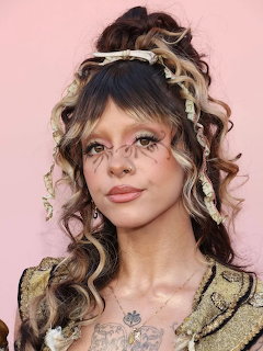 Portrait of a woman with curled hair, face makeup, and a vintage-style dress on a pink background