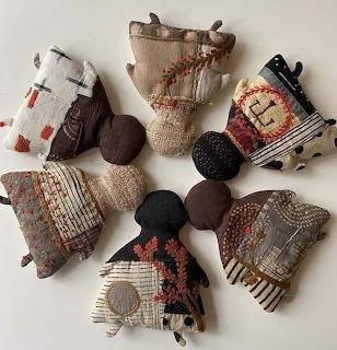 Seven handmade faceless cloth dolls made of patchwork fabric on a white background