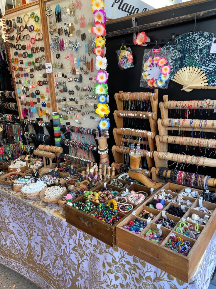 Outdoor jewelry market booth with bracelets, necklaces, earrings, and beads displayed on wooden stands and pegboards.