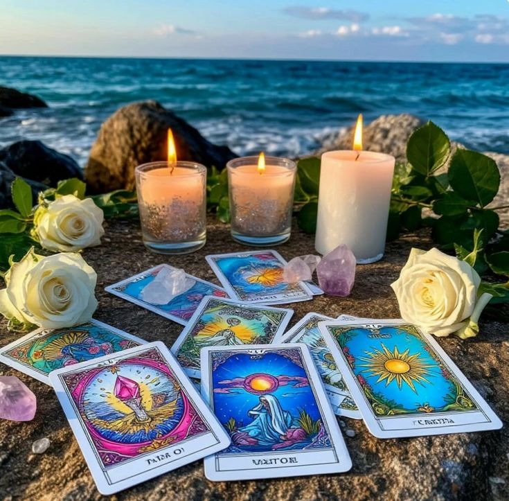 Tarot cards with candles and white roses on beach rocks by the ocean