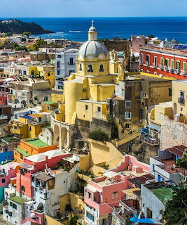 Aerial view of colorful buildings and yellow church dome in Procida, Italy, overlooking the sea