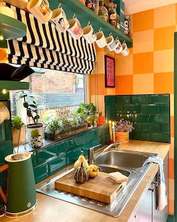 Bright kitchen with green tiles, orange checkered wall, striped window valance, sink and herbs on sill